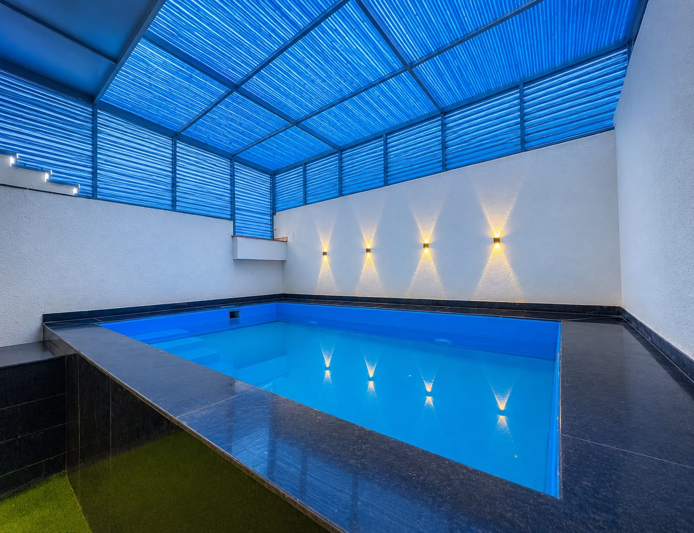 Private pool stay in Jaipur — a large blue pool with black tiled floor and woven roof, serene and contemporary